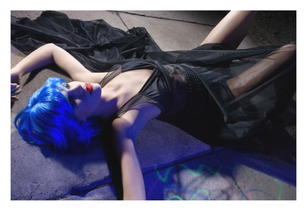 Blue Velvet fine art fashion photograph by LiAns JadAn featuring a model with vivid blue hair reclining on concrete in dramatic directional light