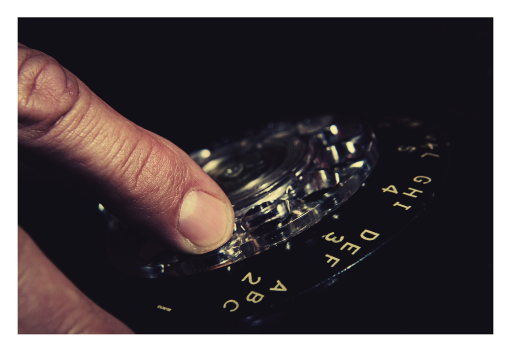 Dial Tone fine art photograph by LiAns JadAn featuring a hand turning the dial of a vintage rotary telephone in dramatic low light