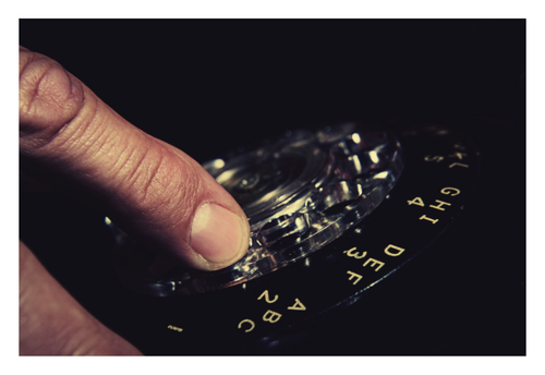 Dial Tone fine art photograph by LiAns JadAn featuring a hand turning the dial of a vintage rotary telephone in dramatic low light